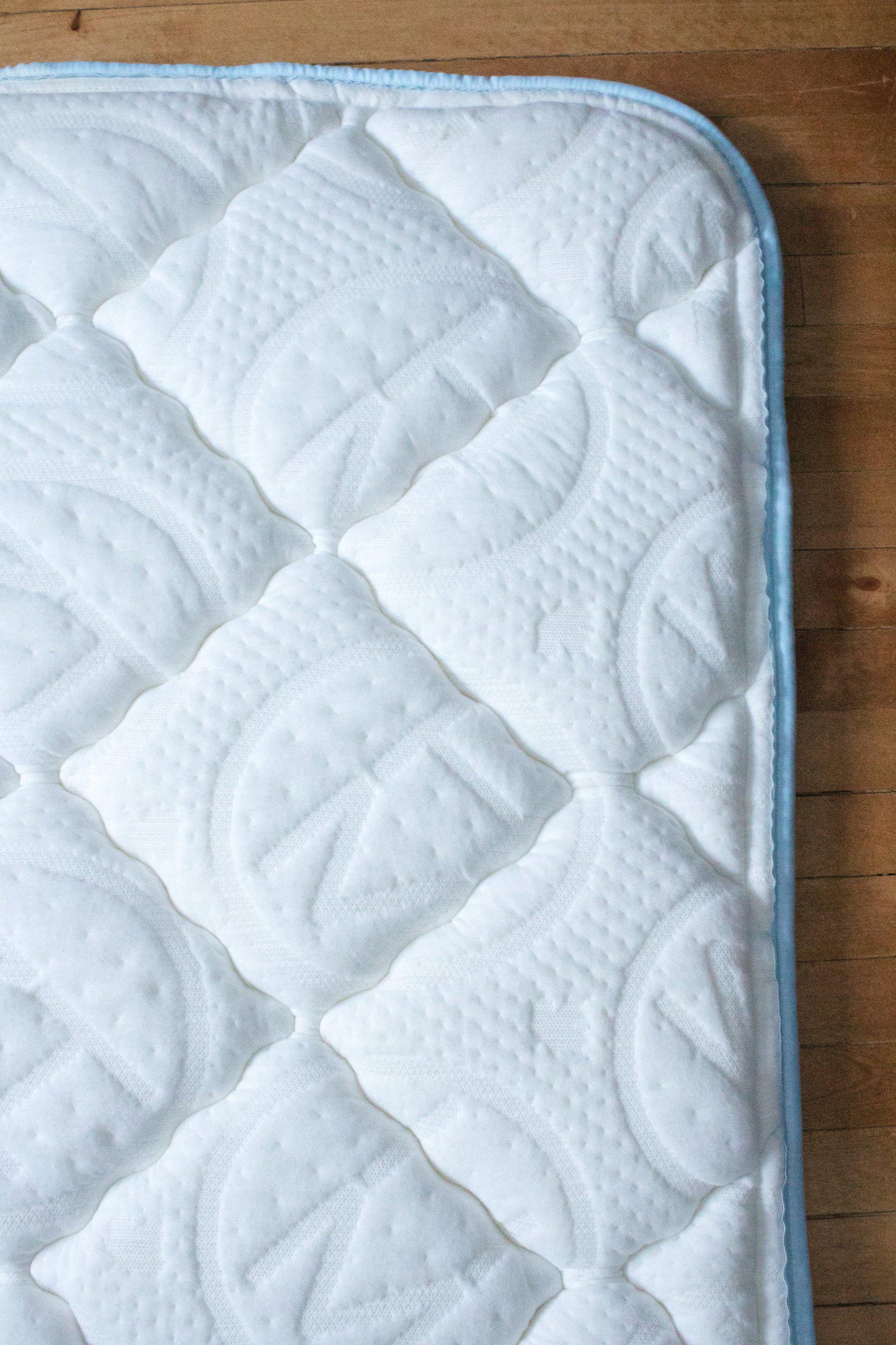 Close up of Haven Soft Comfort Mattress topper on hardwood flooring embossed with the Haven logo to show the thickness