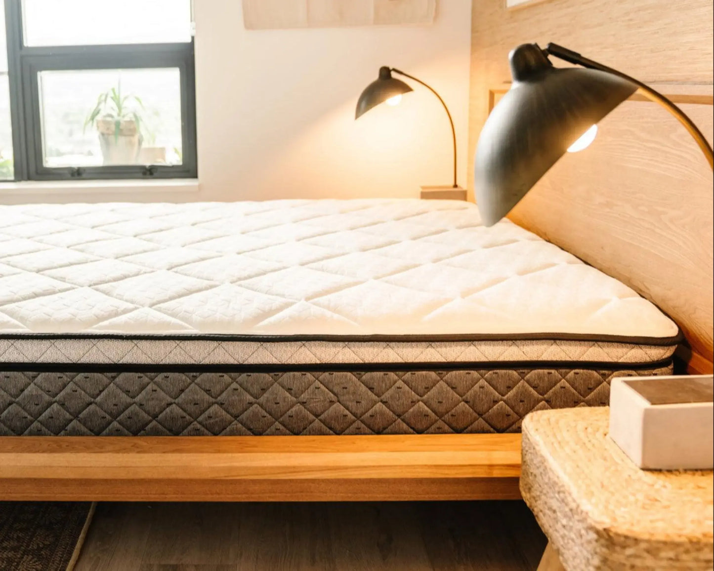 Mattress on a wooden bed frame with lamps and a window in the background