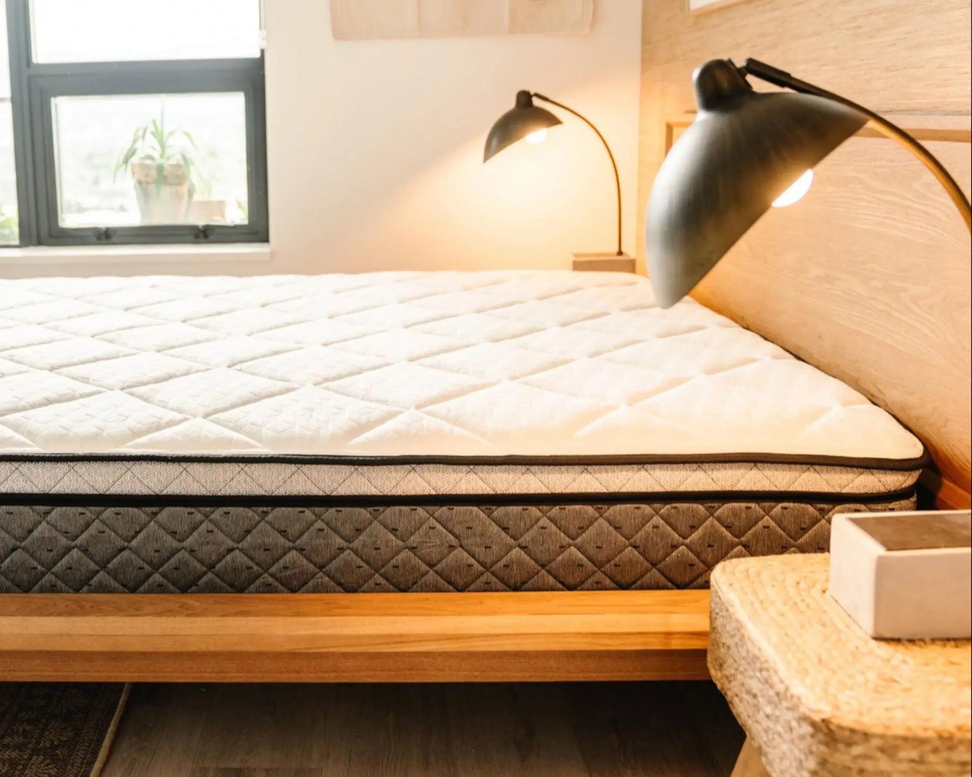 Mattress on a wooden bed frame with lamps and a window in the background